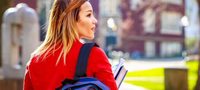 Girl walking outdoors with backpack and books in hand