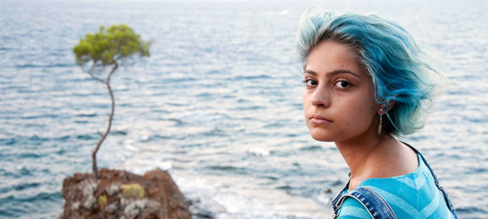Young woman sitting by the ocean with a serious expression