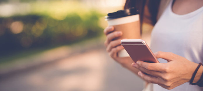 A student holding a coffee and a cellphone
