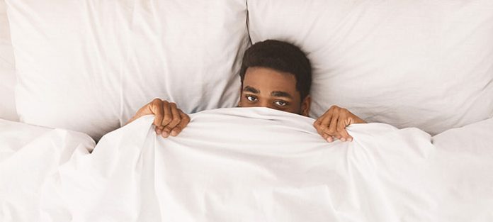 tired male in bed peeking over sheets