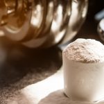 Ask the nutritionist: Scoop of protein powder spilled on surface beside metal weights, symbolizing muscle building and nutrition support.