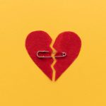 Red felt heart broken in half and pinned together with a safety pin on a yellow background.