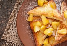 UCookbook: Vegan French toast with apple cinnamon topping Plated vegan French toast topped with warm fruit pieces and powdered sugar on rustic wooden table.