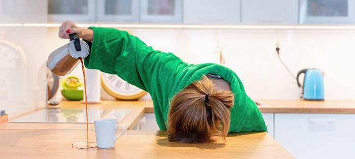 woman with head on kitchen counter, pouring coffee and missing mug | causes of feeling tired all the time