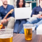 Plastic cups of beer on table with college students socializing in background, representing binge drinking culture.