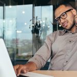 Ask the trainer: A man rubbing his neck while using laptop, showing neck pain from desk work.