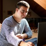 Ask the professor: “How do you stay motivated through summer classes?” Young man with down syndrome using laptop indoors | tips to stay motivated in college