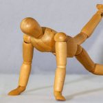 Wooden mannequin posed in a push-up position with one leg raised, mimicking exercise form.