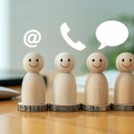 Wooden figurines with smiley faces on a desk, with icons for email, chat, and phone above them.