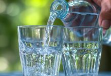 Ask the doc: “When can drinking too much water be dangerous?” Water being poured from bottle into two glasses outdoors, illustrating hydration and fluid intake awareness.