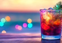 3 festive mocktail recipes to liven up the holidays Colorful sparkling drink with ice, lime, and pine garnish against a blurred festive background.
