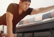 Man balancing on one leg and arm while exercising indoors, following instructions from laptop screen.