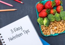 A lunchbox with strawberries, broccoli, nuts, and a notebook saying “3 Easy Nutrition Tips.”