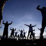 FitnessU: Pyramid training A group of people exercising outdoors together, silhouetted against a bright and colorful sunset.