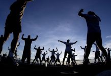 A group of people exercising outdoors together, silhouetted against a bright and colorful sunset.
