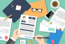 “Top-down view of hands reviewing resume among various office documents, charts, glasses, and coffee.”