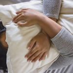 A person lying in bed, covering their face with a pillow, appearing stressed or frustrated.