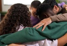 A group of four people embracing in a supportive huddle, symbolizing unity and comfort.