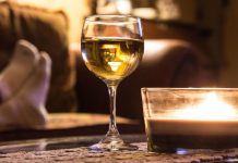 A glass of white wine and a lit candle on a table, with someone relaxing in the background.
