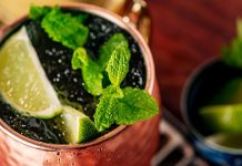 Copper mug filled with ice, lime slices, and mint leaves on a wooden table setting.