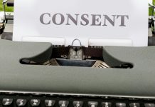 Close-up of a typewriter with a paper showing the word 'Consent' outdoors on a grassy surface.