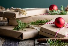 Neatly wrapped holiday gifts with twine, red ornaments, and greenery on a rustic wooden surface.