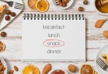 Open notebook with "snack" circled, surrounded by pie slices, nuts, dried oranges, and almonds on a table.