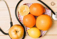 A stethoscope next to a plate of citrus fruits and an apple on a wooden table.