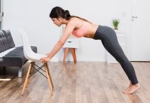 Person doing an incline push-up at home using a chair, dressed in activewear, in a bright room.