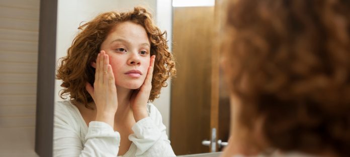 Young woman with freckles looking in mirror