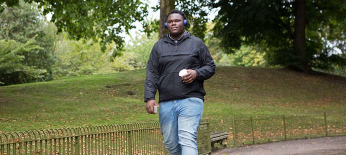 Guy walking through a park with headphones and a coffee