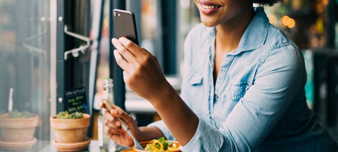 african american young woman eating while looking at phone