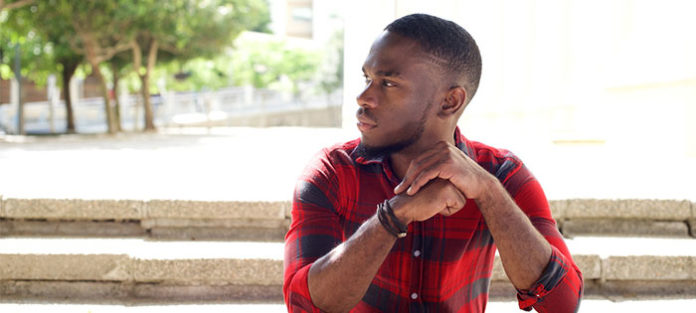 Young man sitting on a step outside looking to the left