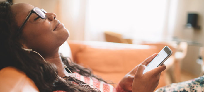 young black female relaxing with earbuds and mobile device
